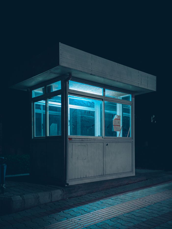 Modern glass security booth lit up at night, showcasing urban design and architecture.