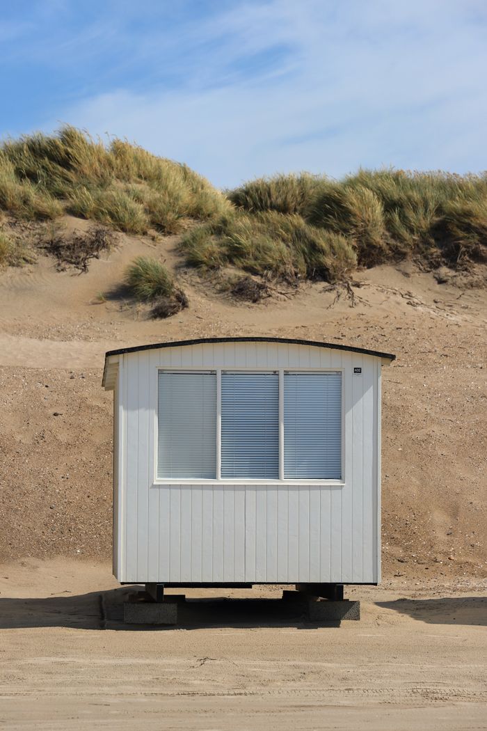 White beach hut nestled against Danish dunes under blue skies, capturing summer's essence.